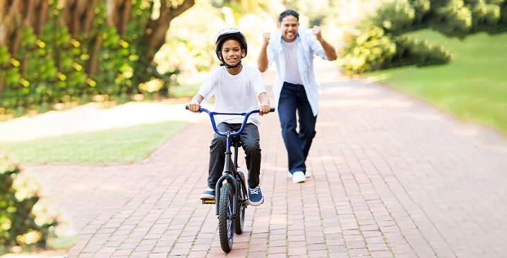 Excited father teaching boy to ride a bike